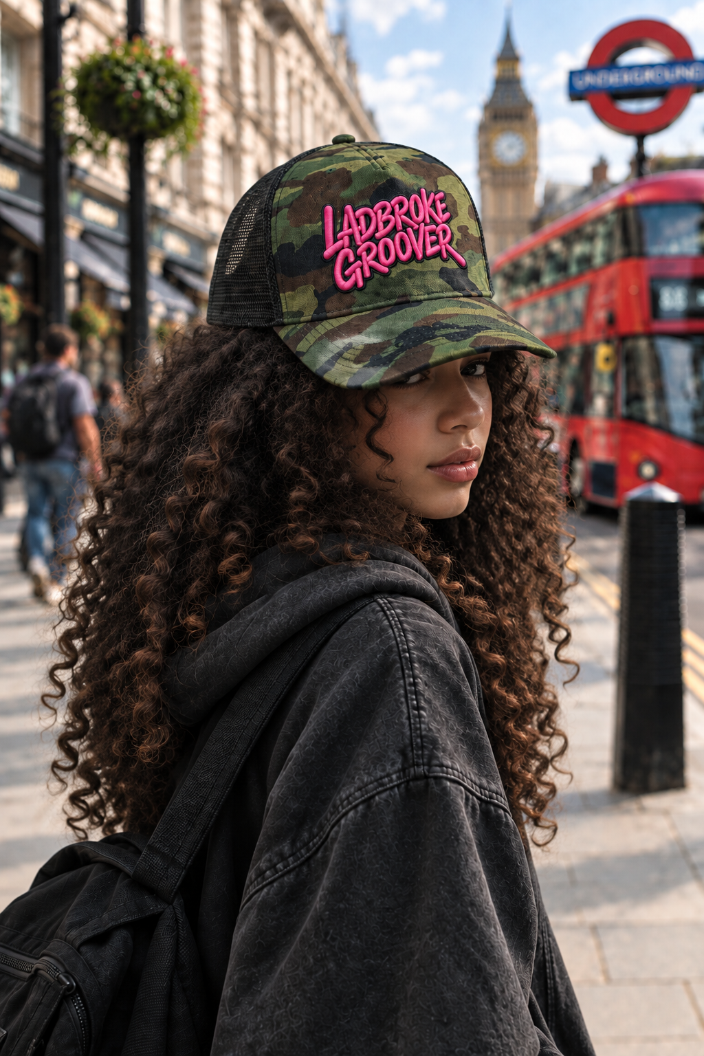 Young model with curly hair in slight profile wearing a pink embroidered camo Ladbroke Groover cap